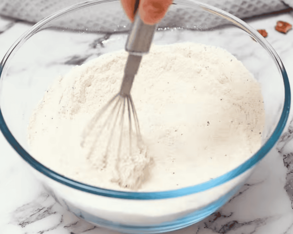 A glass mixing bowl filled with dry ingredients being whisked together to combine them evenly.