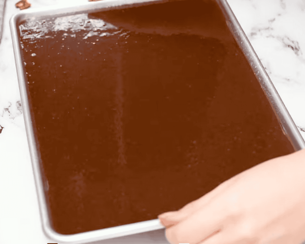 A baking sheet filled with smooth, dark chocolate cake batter, ready to be baked.