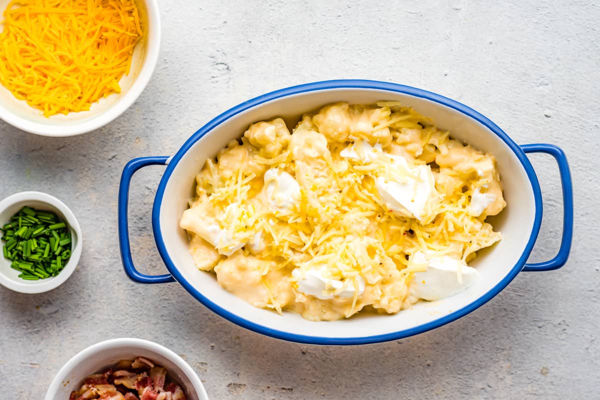 Cheesy cauliflower in a baking dish, topped with dollops of sour cream.