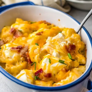 close up of loaded cauliflower bake in a blue and white casserole dish with a spoon.