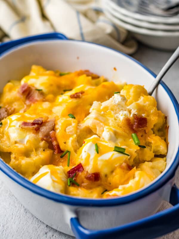 close up of loaded cauliflower bake in a blue and white casserole dish with a spoon.