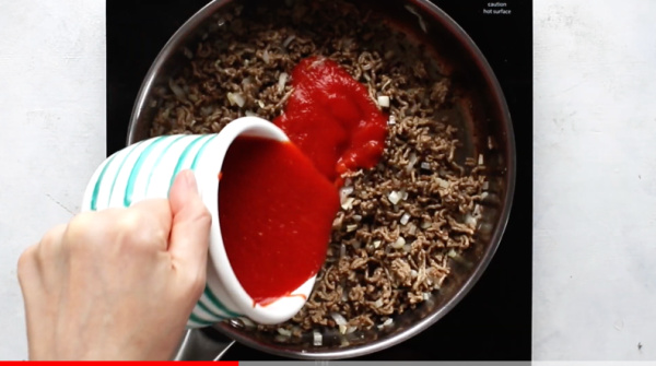 pouring marinara sauce into saucepan with ground beef, onions, and garlic