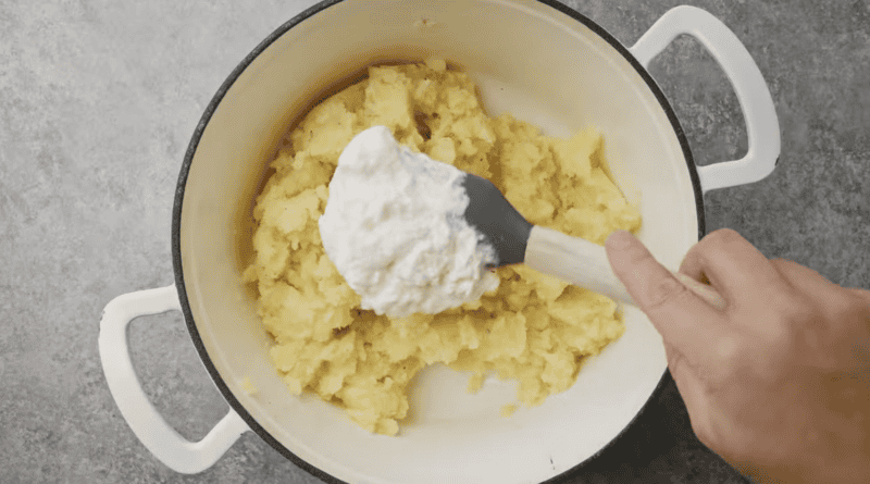 placing whipped cream on top of mashed potatoes with a rubber spatula.