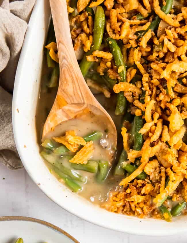 green bean casserole in a white casserole dish with a wood spoon