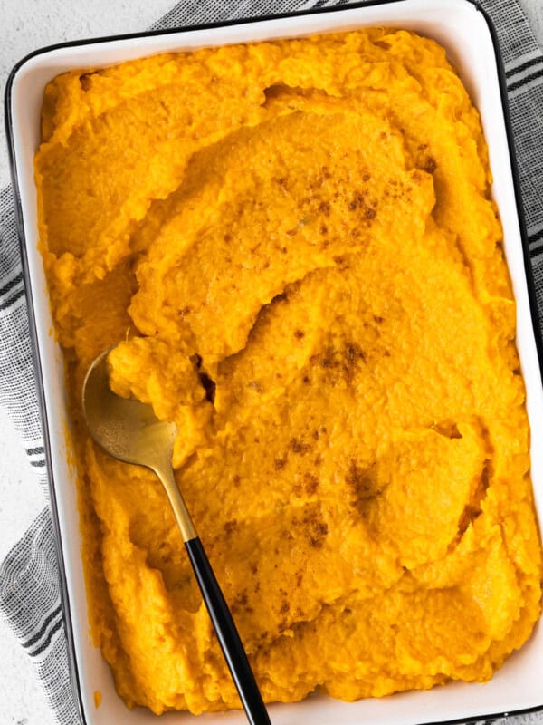 mashed sweet potatoes in a white rectangle baking dish with a serving spoon