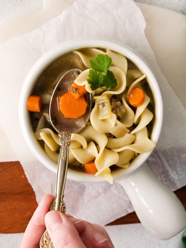 turkey noodle soup in a white bowl with a hand holding a spoon