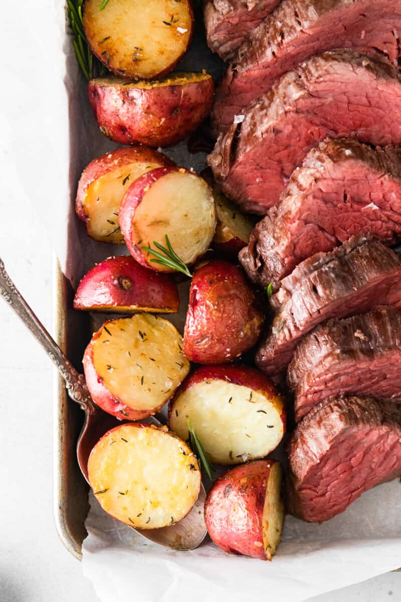 roasted red potatoes and sliced beef tenderloin on a sheet pan with a serving spoon