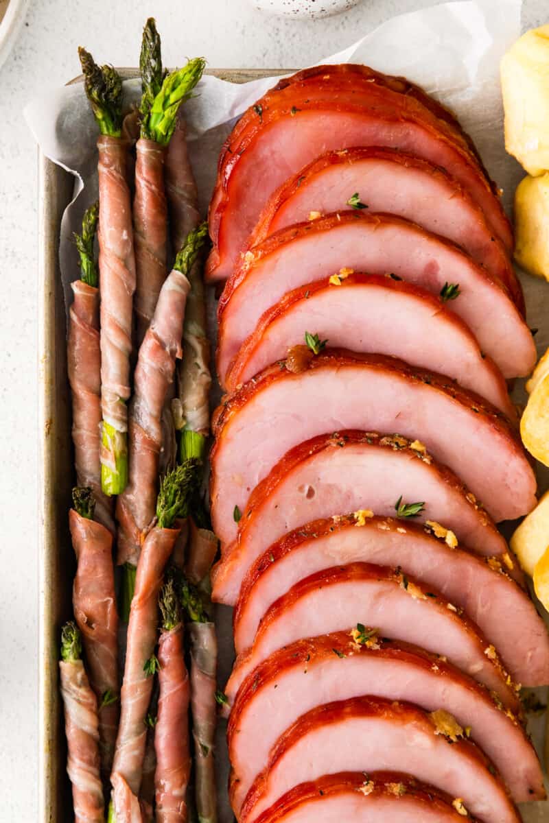 slices of brown sugar ham and prosciutto wrapped asparagus spears on a sheet pan