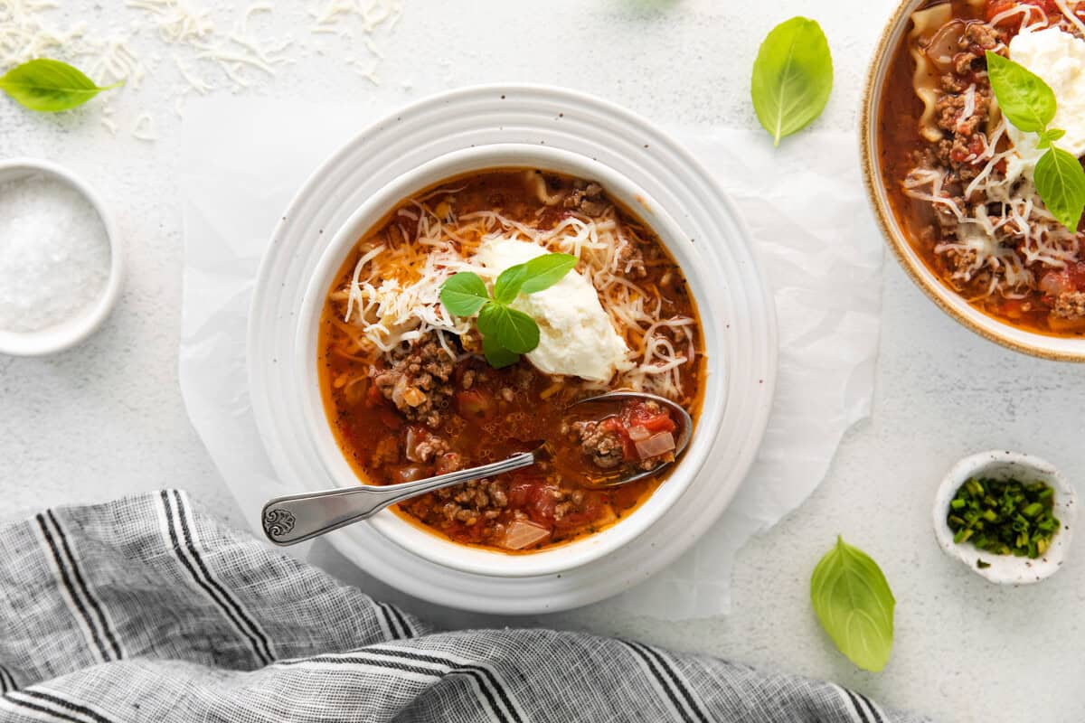 lasagna soup topped with ricotta cheese, parmesan cheese, and basil in a white bowl