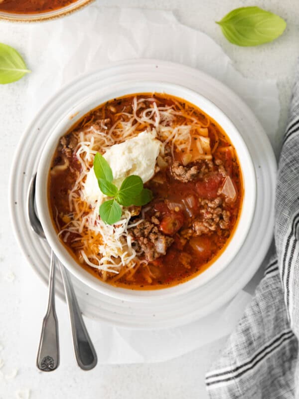 lasagna soup topped with ricotta cheese, parmesan cheese, and basil in a white bowl