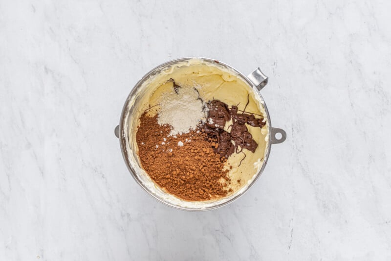 cocoa powder, melted chocolate, and flour added to cheesecake batter in a metal bowl