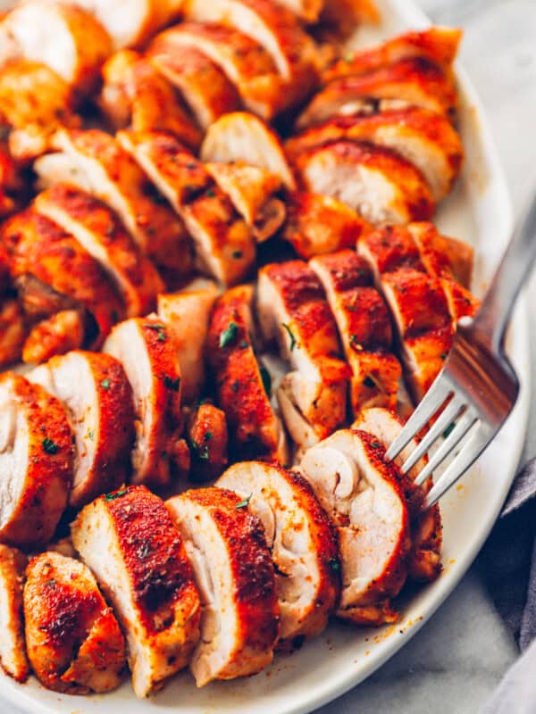 sliced baked chicken thighs on a white serving tray with a fork in one