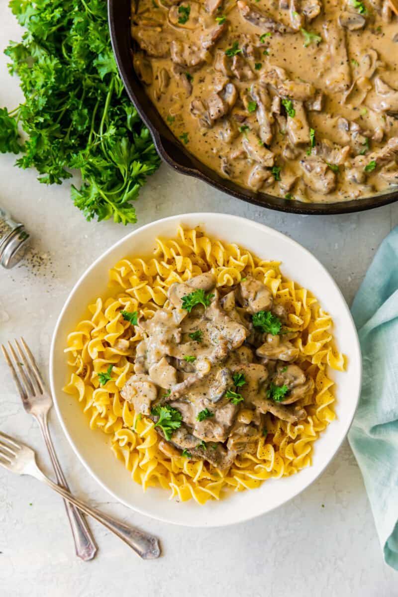 overhead image of noodles topped with beef stroganoff in a white bowl with 2 forks