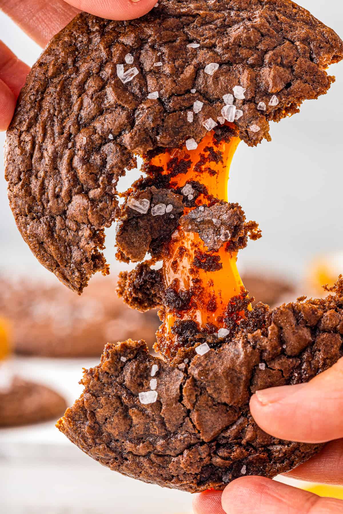 hands breaking a chocolate cookie in half showing the gooey caramel center.