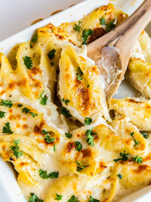 pasta shells stuffed with cheese and chicken topped with alfredo sauce in a baking dish with a wood spoon