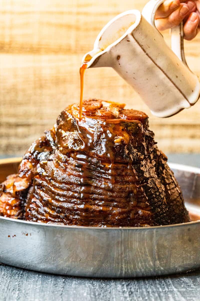 hand pouring glaze onto honey baked ham