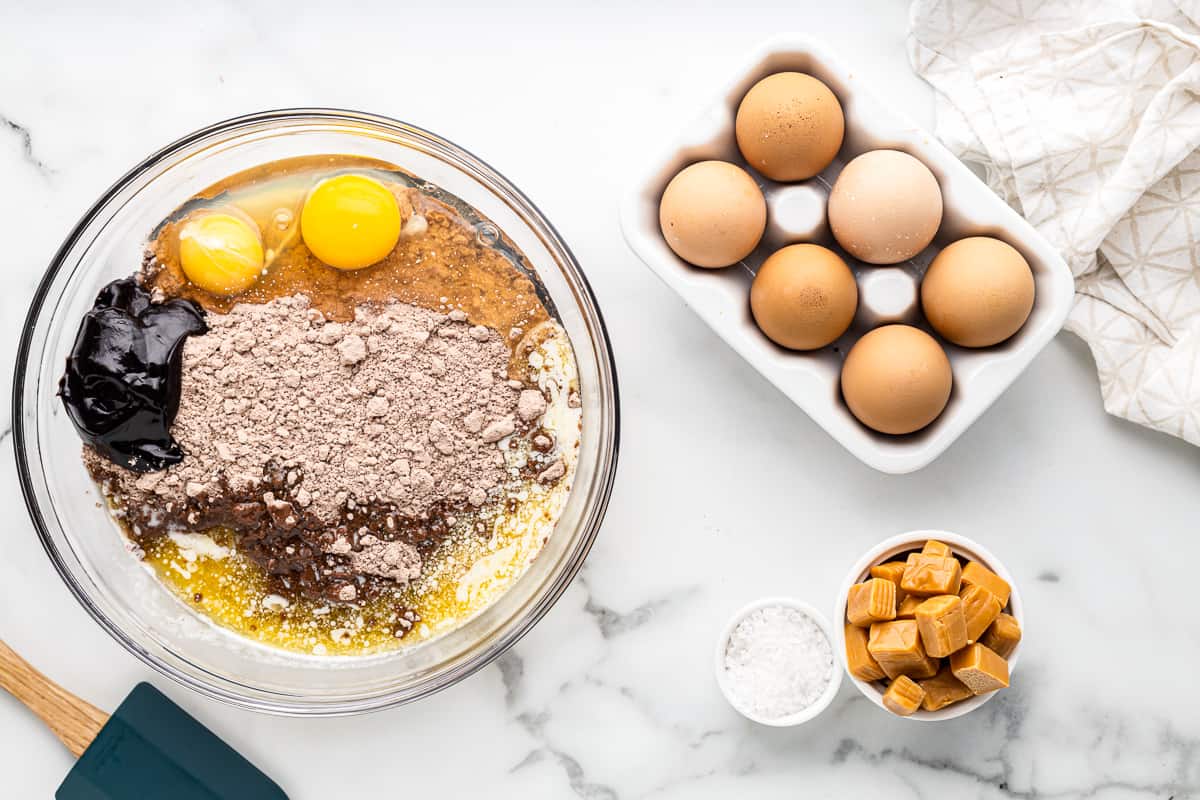 Cookie dough ingredients combined in a glass mixing bowl, next to a bowl of caramels.