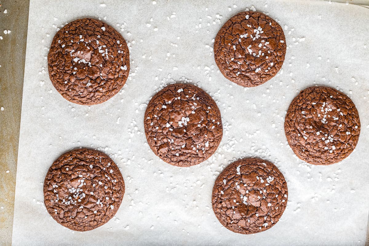 Carmel brownie cookies topped with sea salt on a parchment paper lined baking sheet.