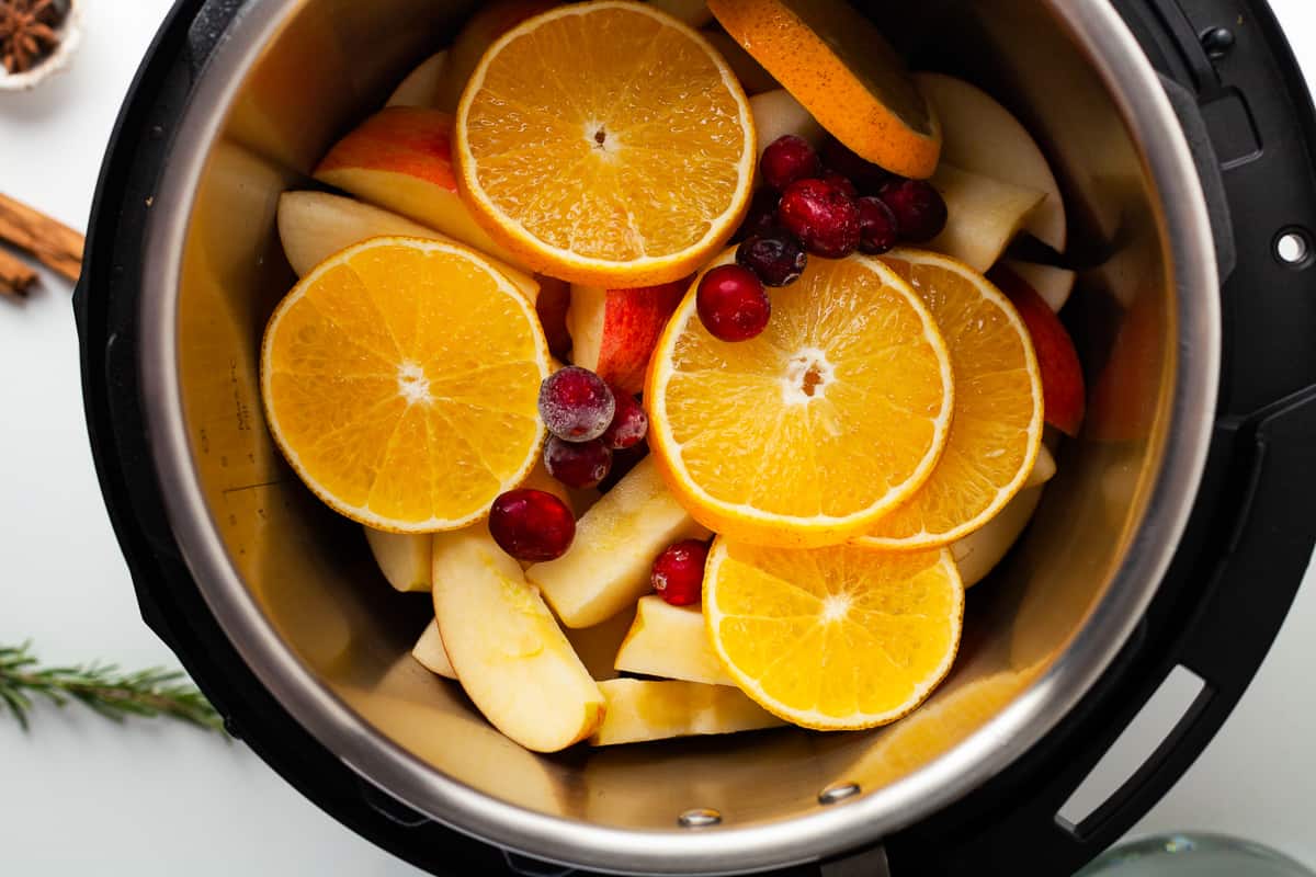 Slices of apple, orange, and cranberries in the pot of a pressure cooker.