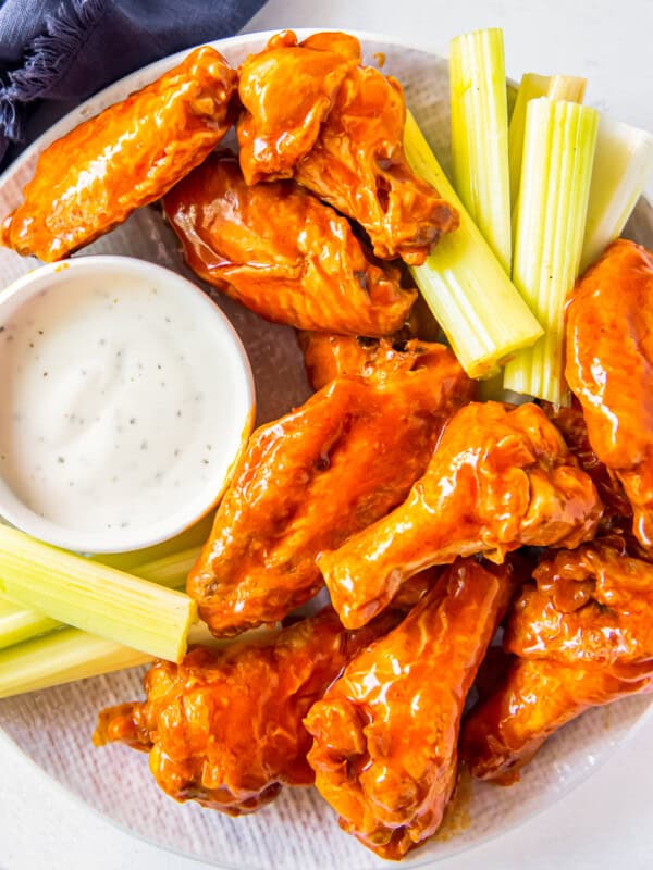 overhead image of buffalo chicken wings, sliced carrots, sliced celery, and dressing in a white bowl on a white plate