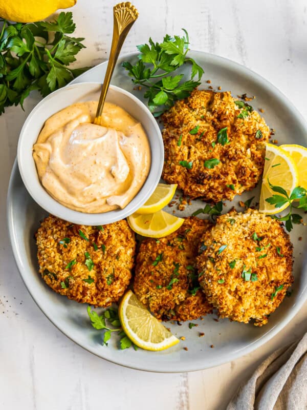 crab cakes on a plate with lemon slices and sauce in a bowl with a spoon