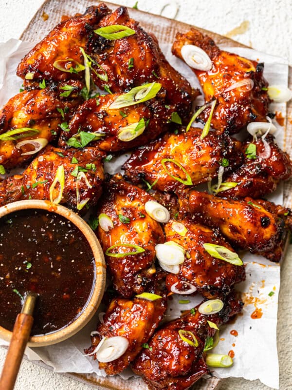 baked korean hot wings on a serving platter with sauce in a bowl with a spoon