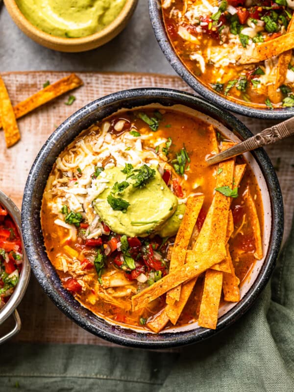 chicken fajita soup in a black bowl topped with cheese, guacamole, diced tomatoes, and tortilla strips with a spoon