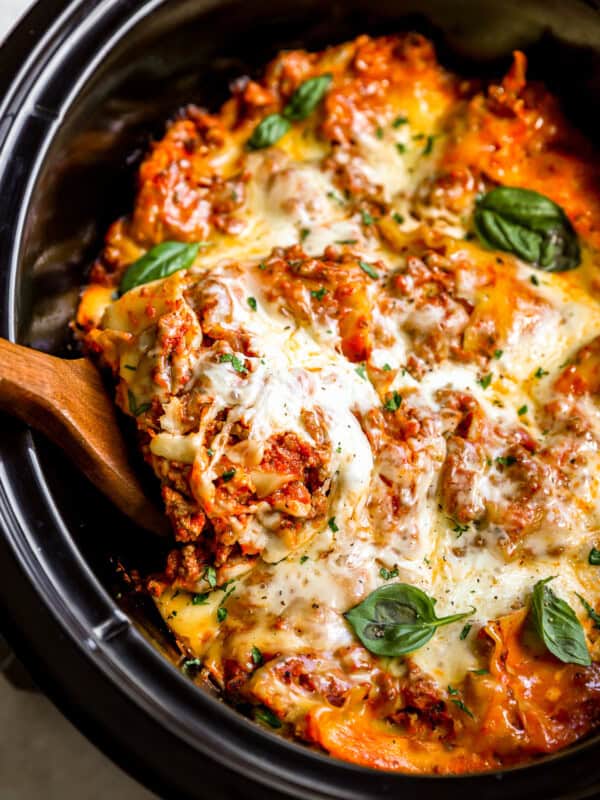 overhead view of a wooden spoon lifting a slice of lasagna from a crockpot.