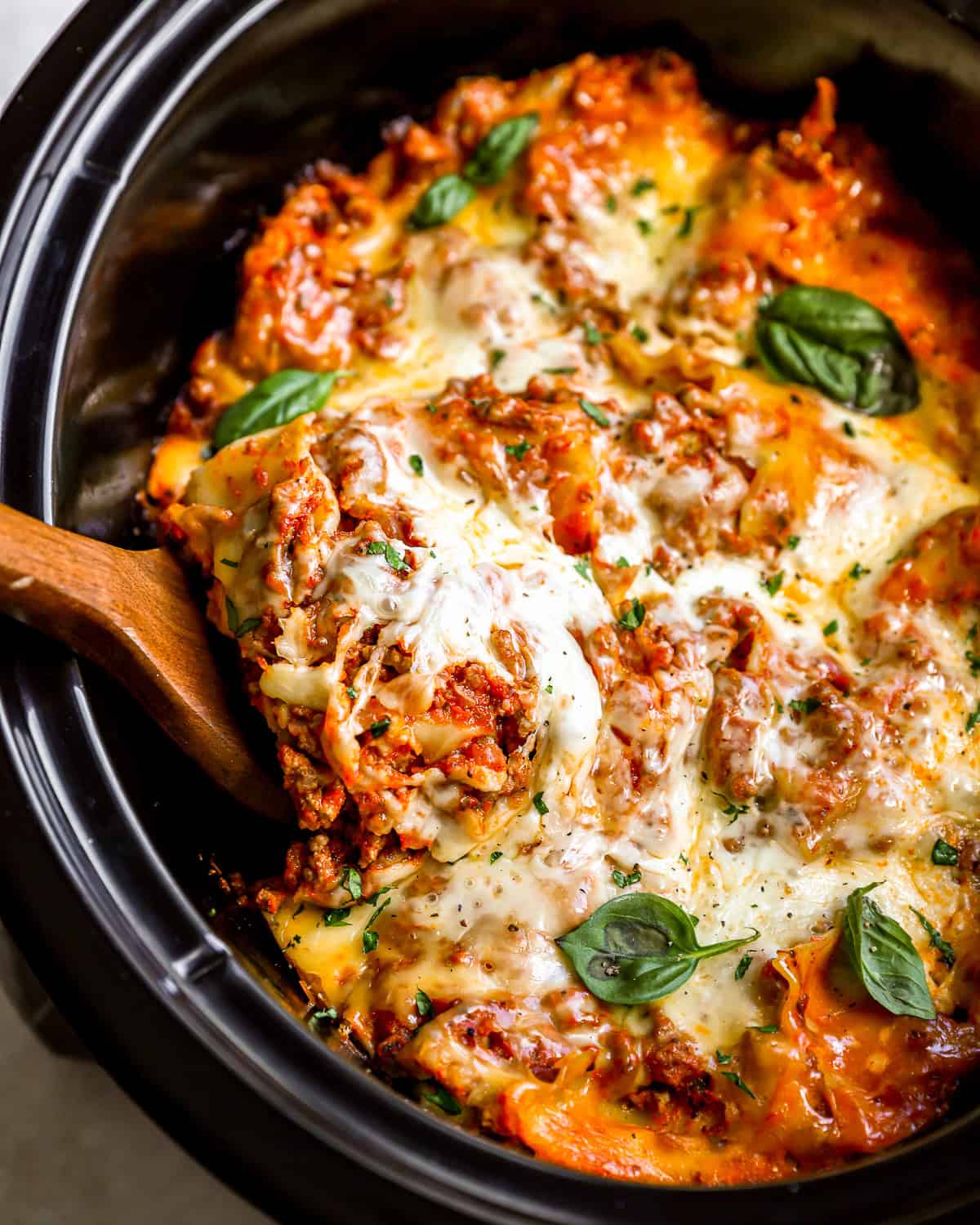 overhead view of a wooden spoon lifting a slice of lasagna from a crockpot.