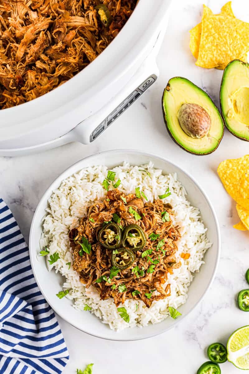 overhead image of shredded salsa chicken and rice topped with jalapeno slices in a white bowl