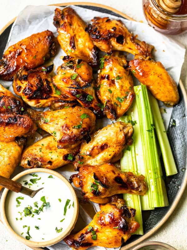 overhead image of hot honey chicken wings and celery slices on a serving tray with ranch dip in a small bowl with a spoon