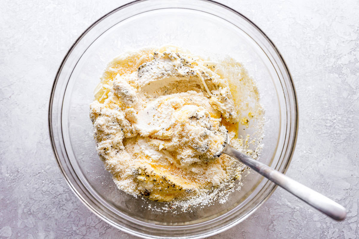 mixing ricotta and shredded cheeses in a glass bowl with a spoon.