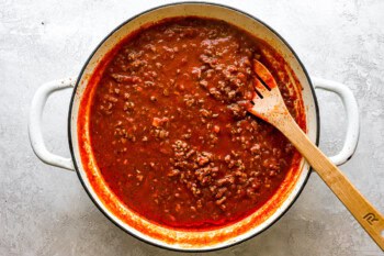 meat sauce in a large pan with a wooden spoon.