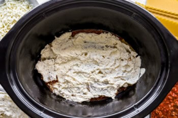 ricotta cheese filling spread over noodles and meat sauce in a crockpot.