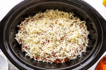 shredded cheese over lasagna in a crockpot.