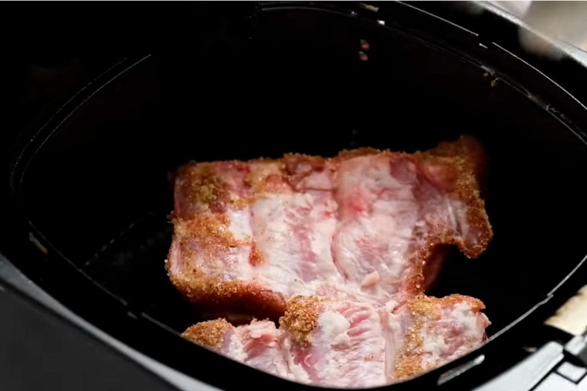 Seasoned ribs are placed carefully in air fryer basket.