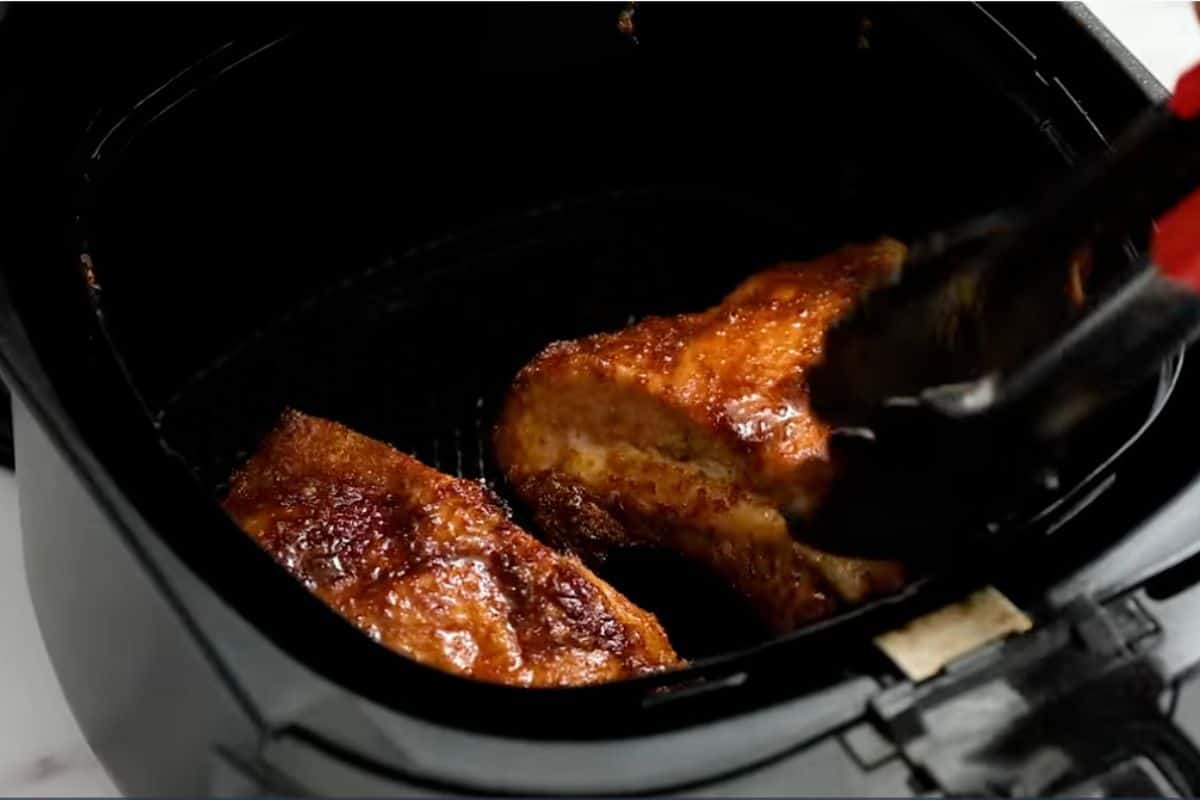 Flipping the bbq ribs after 15 min in air fryer basket with the help of tongs.