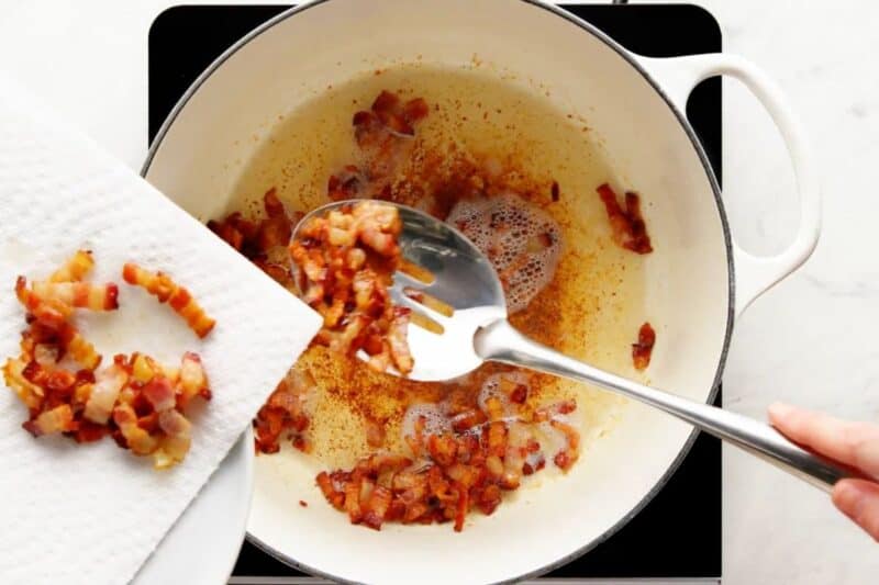 Transferring the cooked bacon on a plate lined with paper towel.