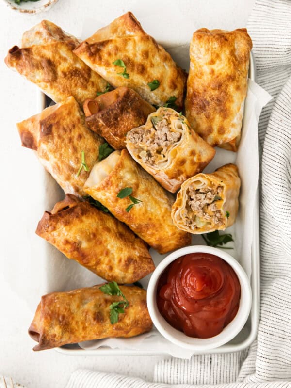 overhead image of cheeseburger egg rolls on a serving tray with a side of ketchup in a white bowl