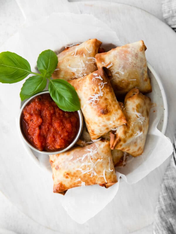 overhead image of pizza rolls in a white bowl with pizza sauce in a metal bowl