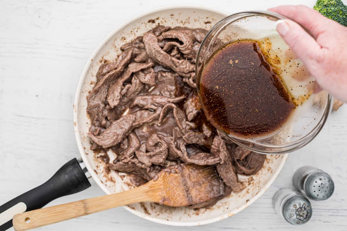 pouring sauce onto steak in a skillet with a wood spoon