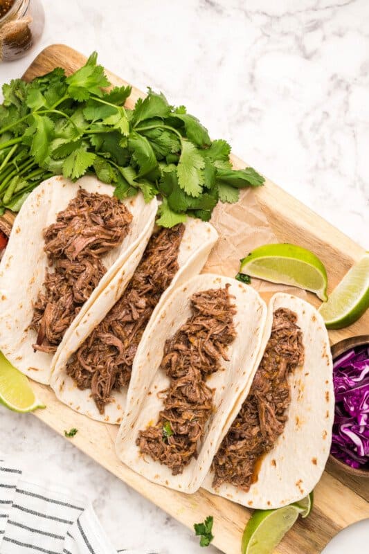 barbacoa meat in flour tortillas on a wood serving board