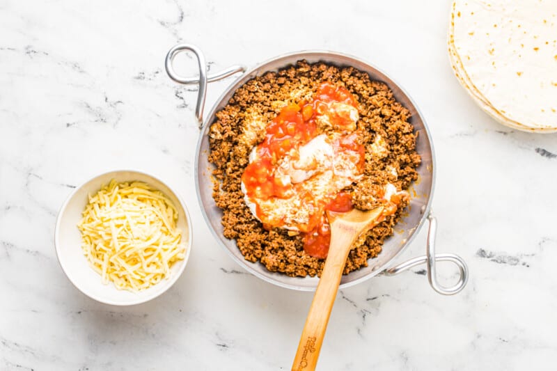 mixing sour cream and salsa into beef filling in a saucepan with a wood spoon