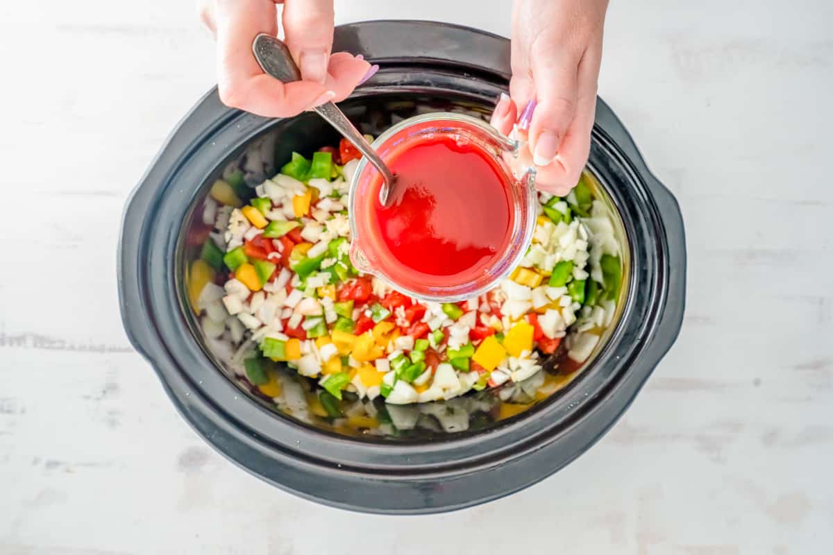 hand spooning wine and tomato sauce mixture on top of chicken and veggies in a crockpot