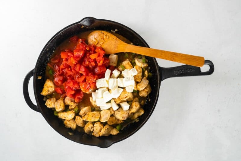 tomatoes and cream cheese in skillet with chicken and wood spoon