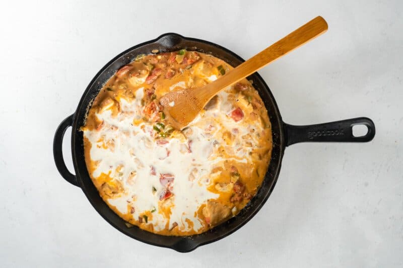 heavy cream added to chicken sauce in skillet with a wood spoon