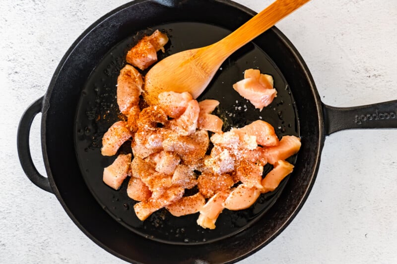 seasoned cubed chicken in a skillet with a wood spoon