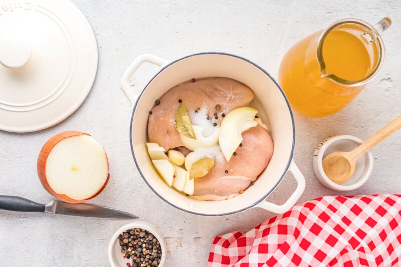 chicken breasts in a pot with bay leaf, salt, peppercorns, and sliced onion