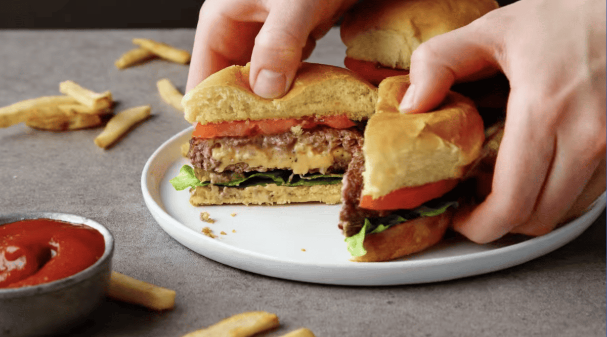 pulling apart a juicy lucy burger to show the molten cheese middle.