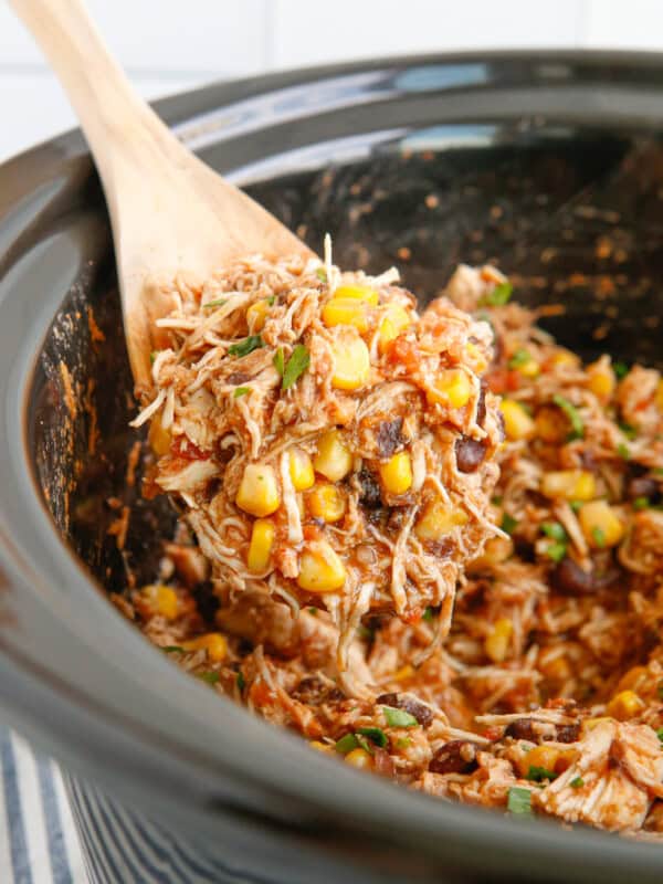 close up of crockpot mexican shredded chicken in a crockpot with a wooden spoon.